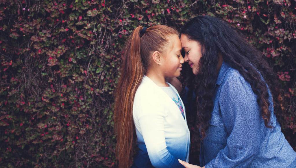 A mother and daughter leaning in tenderly, touching foreheads and noses. 