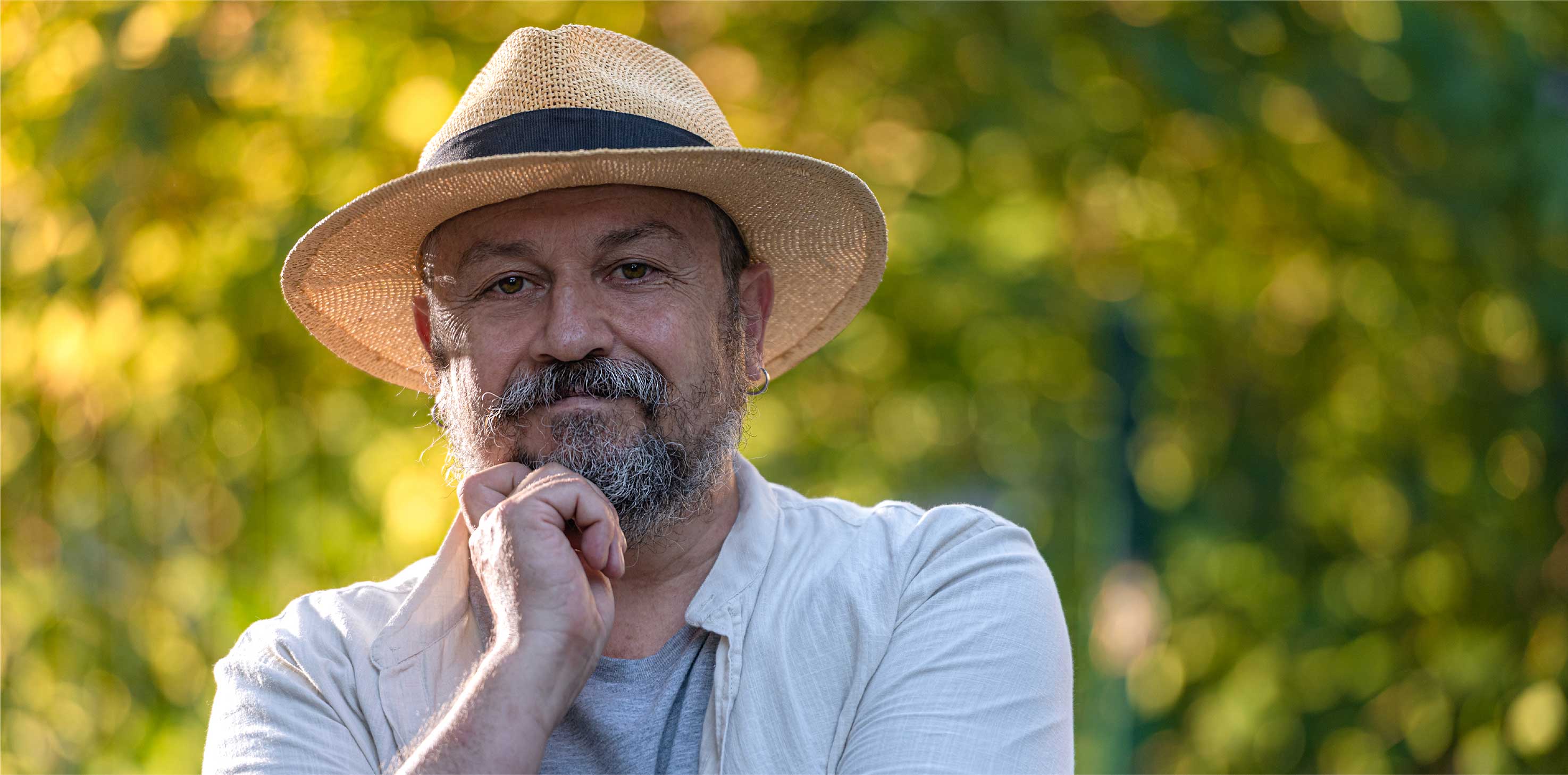 A headshot of a middle-aged Caucasian man, wearing a straw hat, smiling softly at the camera.