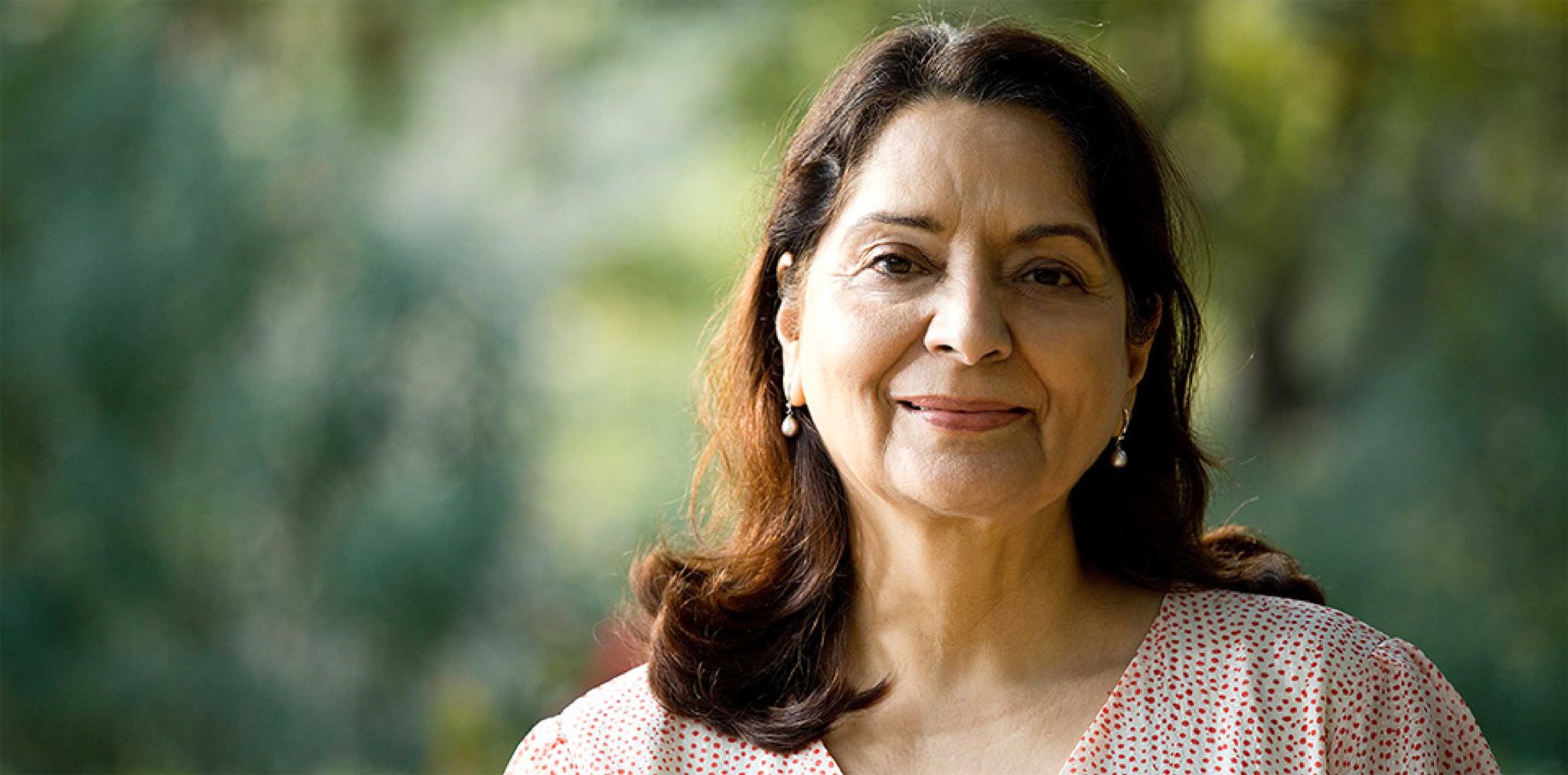 A headshot of a senior woman of South Asian descent, smiling softly at the camera. 