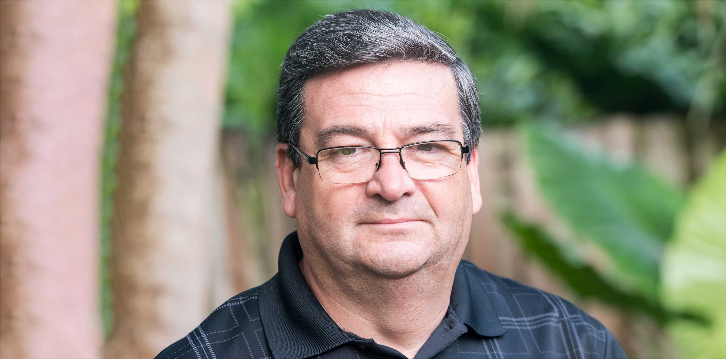 A headshot of a middle-aged Caucasian man, wearing glasses, smiling softly at the camera.