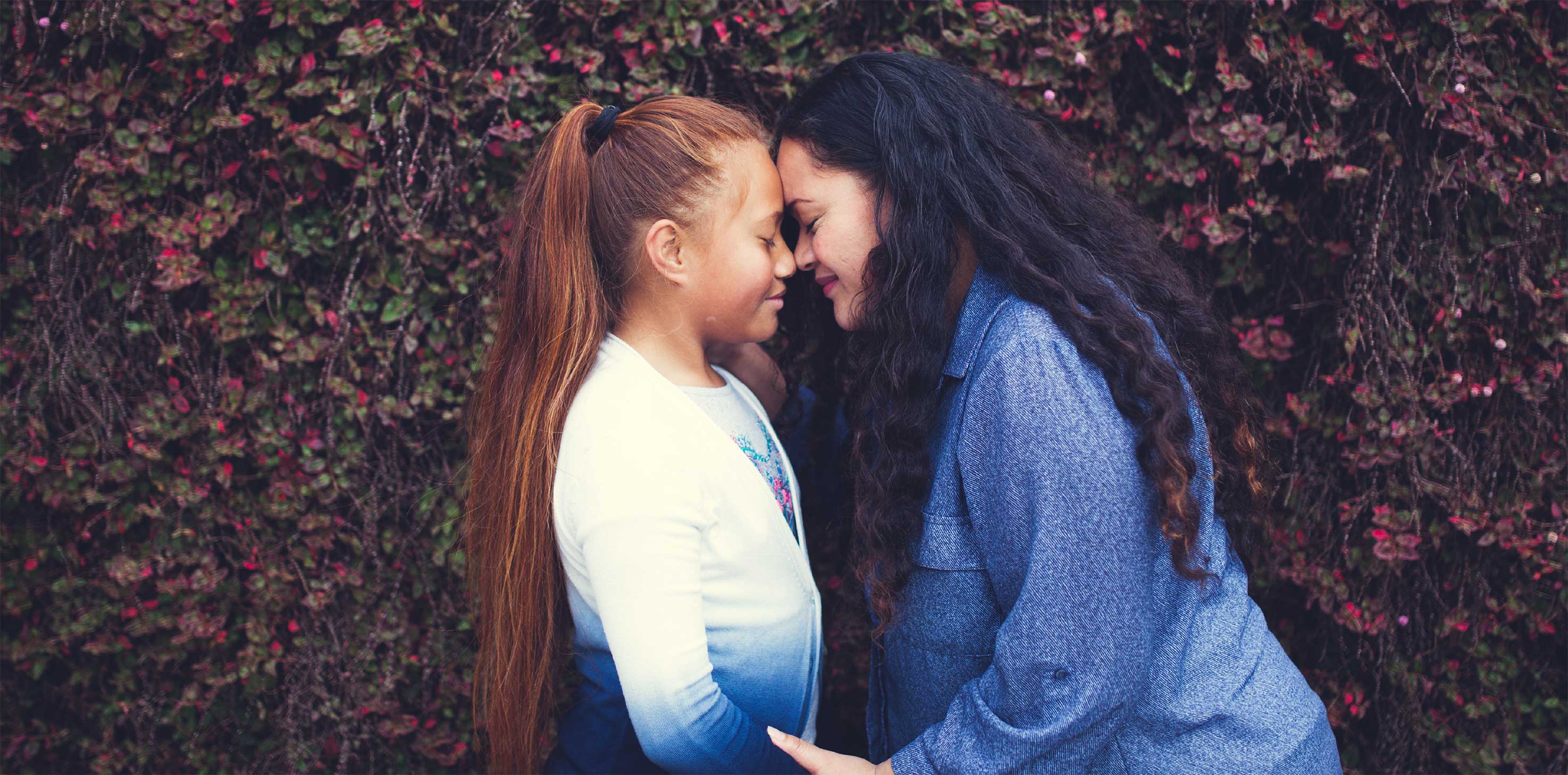 A mother and daughter leaning in tenderly, touching foreheads and noses.