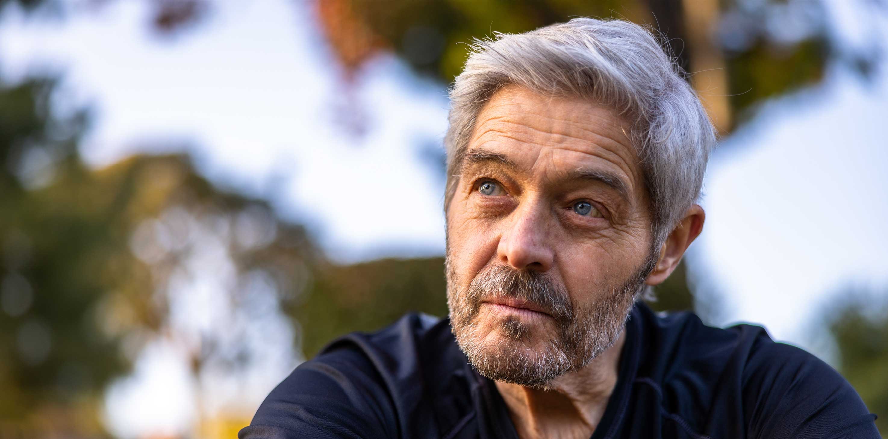 A headshot of a grey-haired Caucasian man, looking pensively off into the distance.