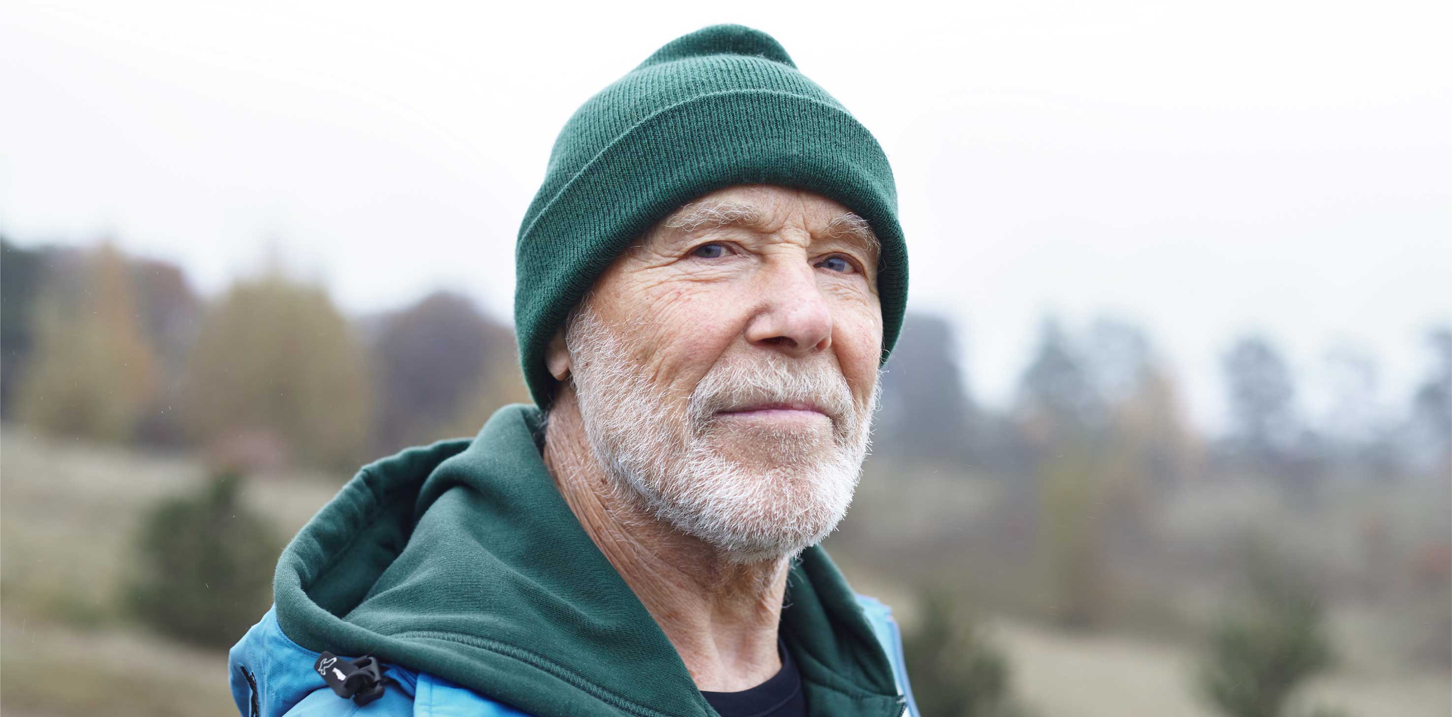 A headshot of an elderly Caucasian man, wearing a beanie and smiling softly at the camera.