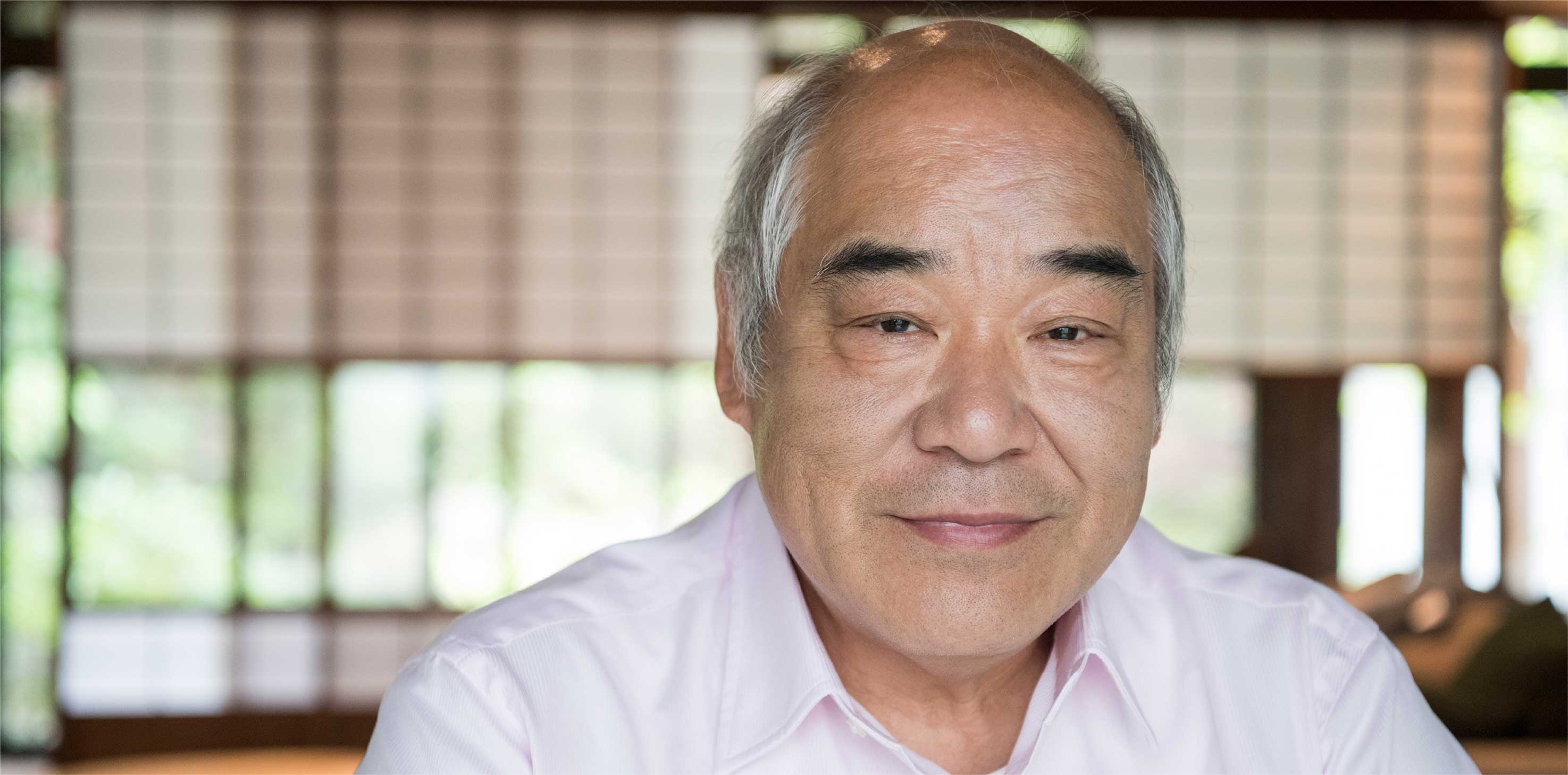 A headshot of a grey-haired man of Asian descent, smiling softly at the camera.