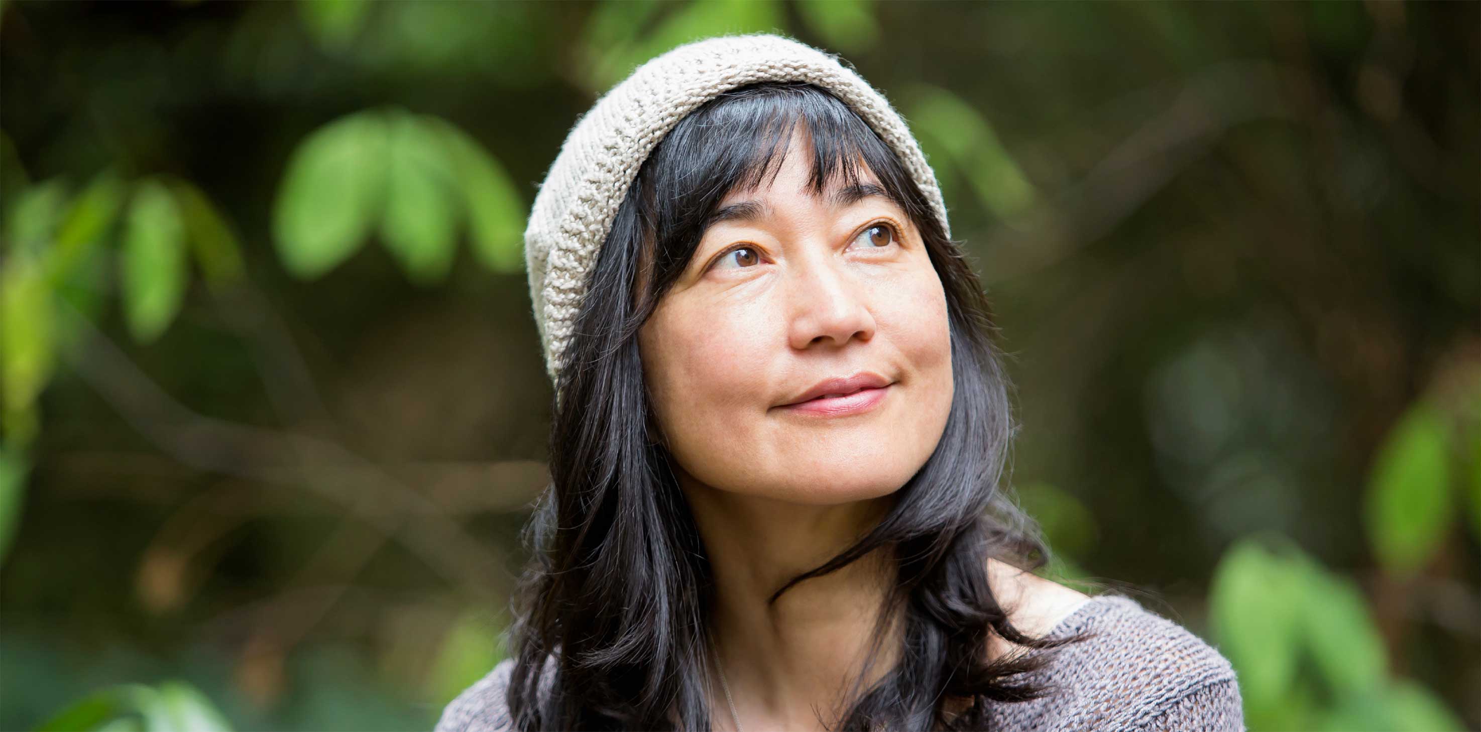 A headshot of a woman of Asian descent, wearing a beanie, smiling softly as  she gazes off into the distance. 